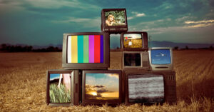 Several televisions stacked on top of one another in a field.