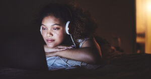 Young woman wearing headphones binge-watching a show on her laptop.