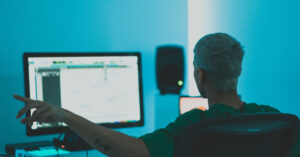 man sitting in front of computer screen producing music