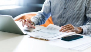 Asian businessman using computer laptop working and reviewing document reports at office workplace. legal expert, professional lawyer reading and checking financial documents or insurance contract