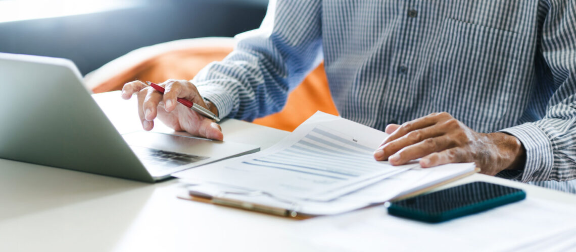 Asian businessman using computer laptop working and reviewing document reports at office workplace. legal expert, professional lawyer reading and checking financial documents or insurance contract