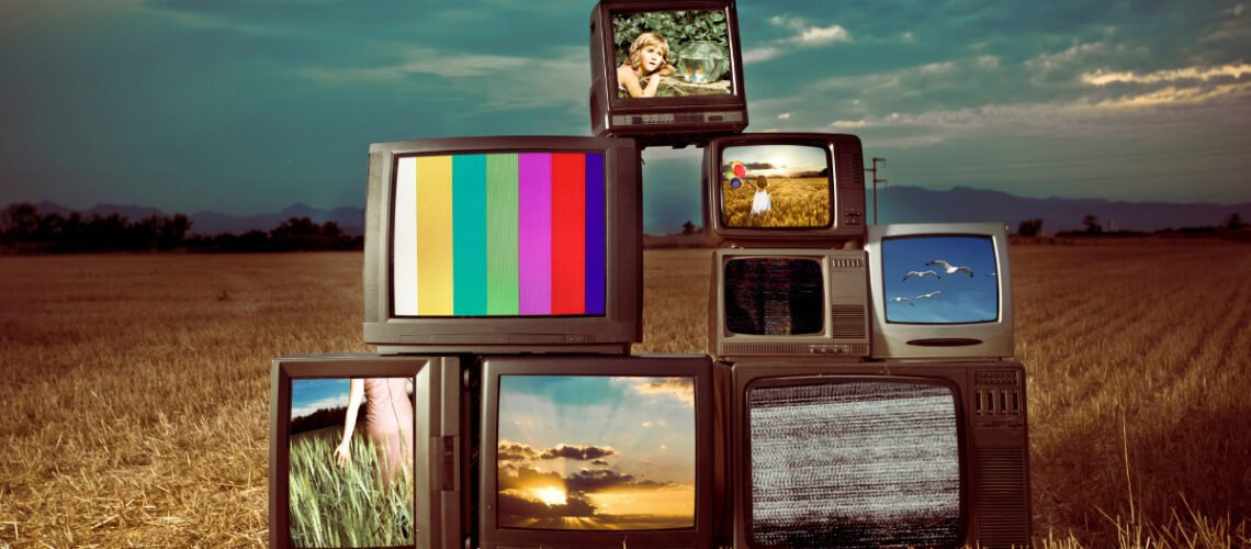 Several televisions stacked on top of one another in a field.