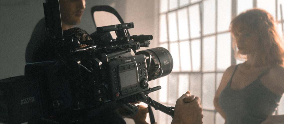man filming woman with camera, windows in the background