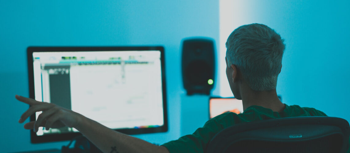 man sitting in front of computer screen producing music